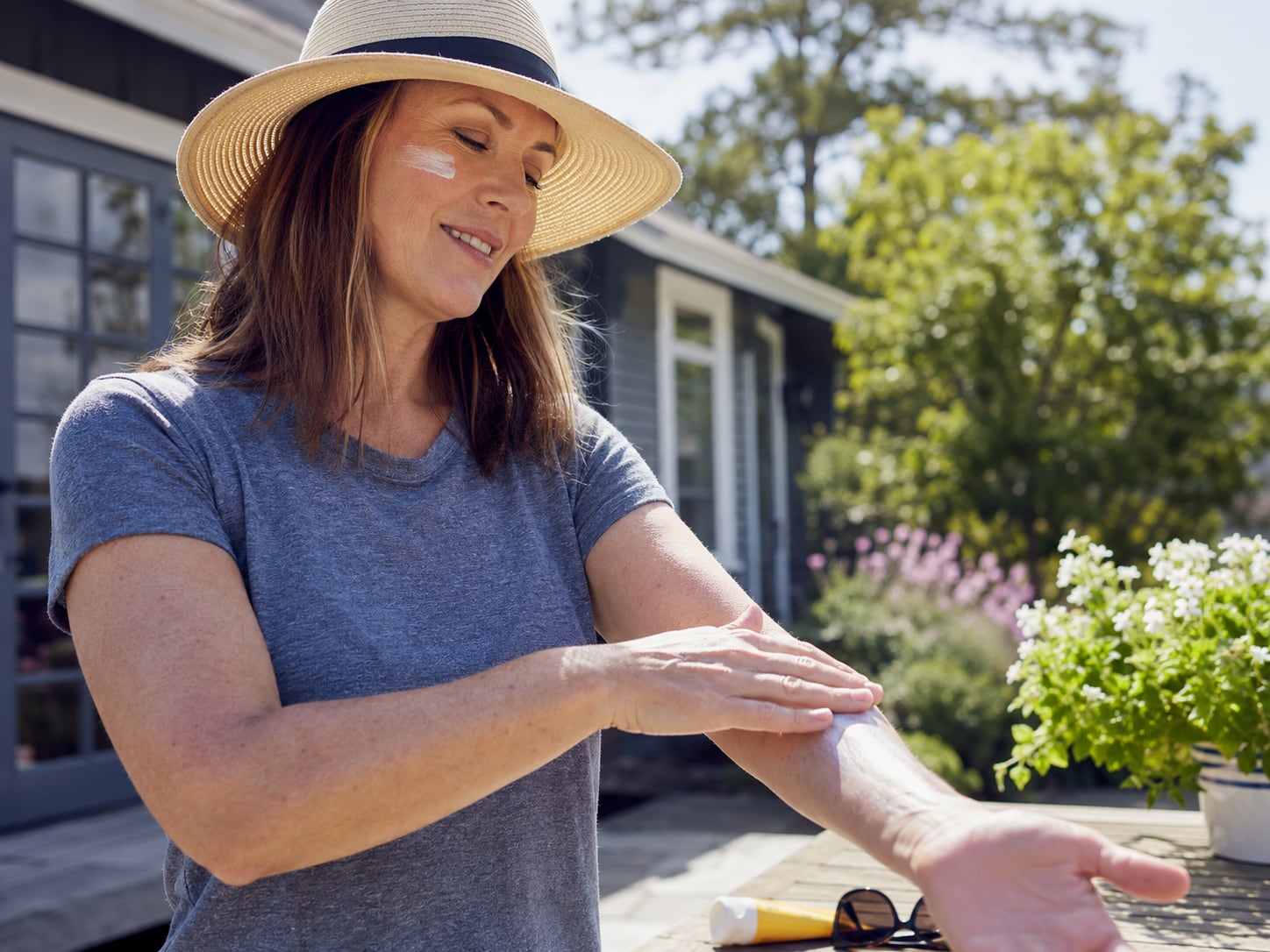 A woman in a sunhat rubs lotion into her hands outdoors in a garden