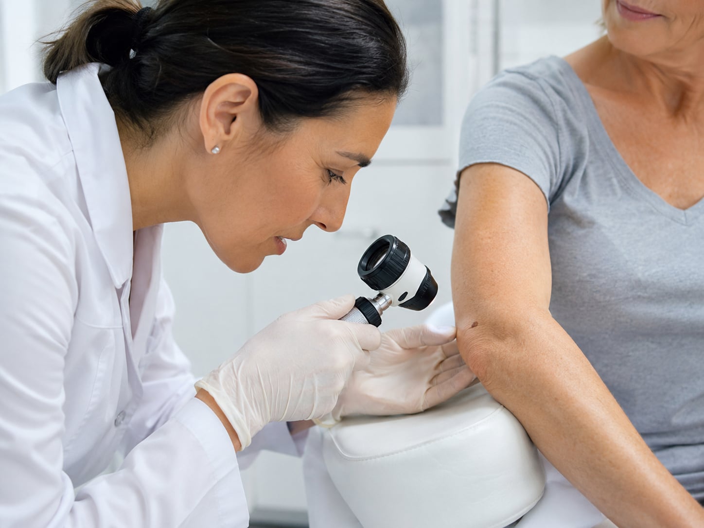 A woman closely examines skin on her arm with a handheld dermatoscope