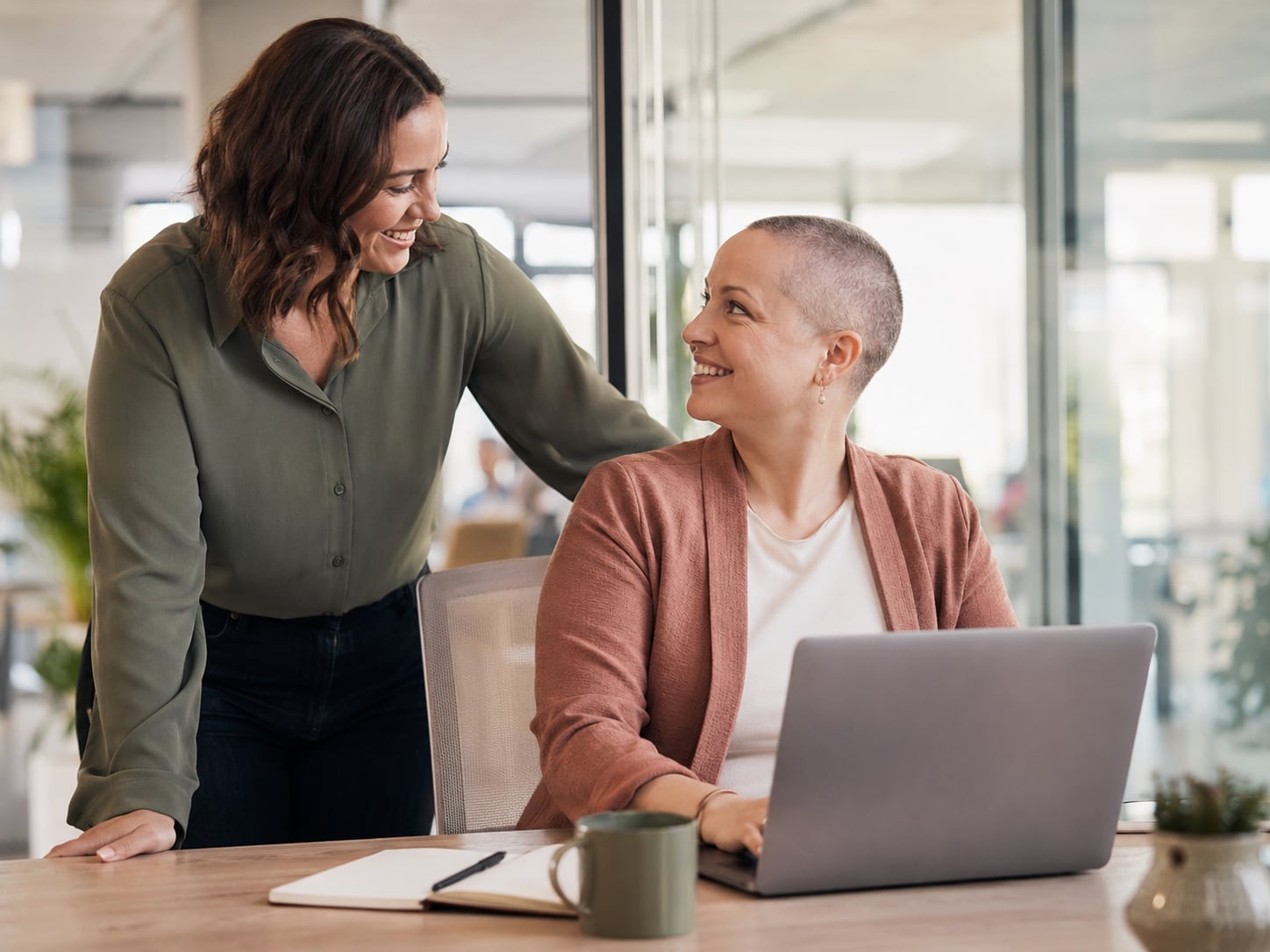 A woman in headscarf and younger woman embrace warmly near a laptop