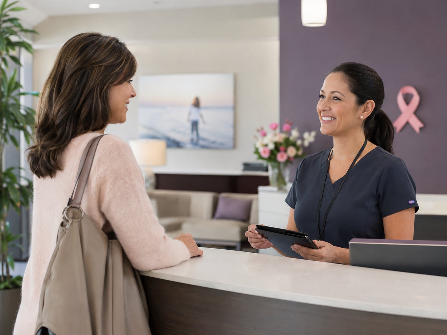 A woman walks toward a reception desk where a smiling staff member greets her