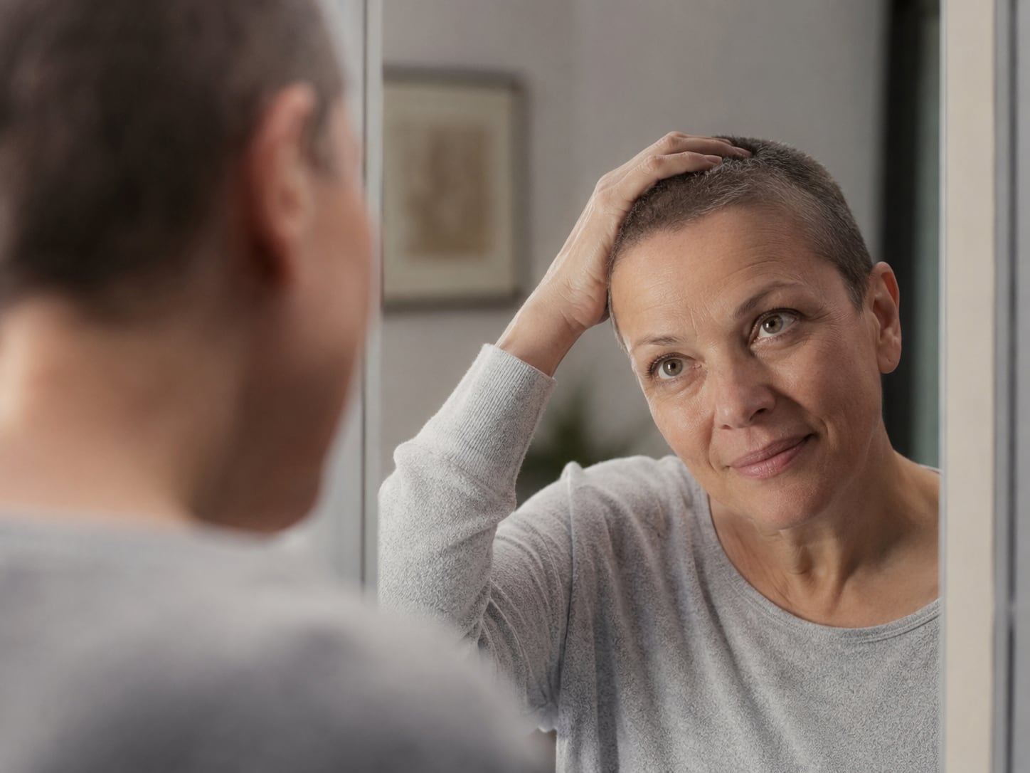 A woman with a shaved head rests her hand on her head, looking upset