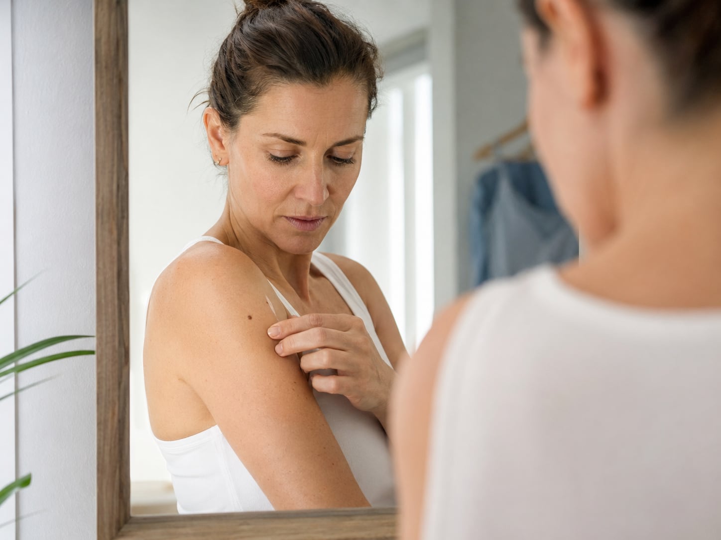 A woman touches and examines her own shoulder and chest closely
